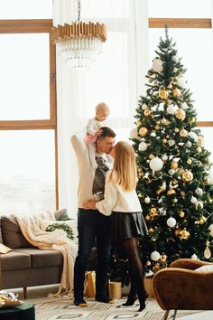 a man and woman holding a baby in front of a christmas tree with a little boy on his lap