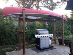 an outdoor grill with a red cover on it's roof next to a wooden deck