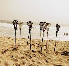 four lacrosse sticks sticking out of the sand at the beach with people in the water behind them