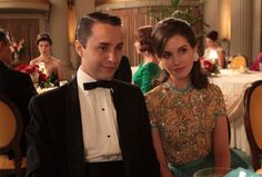 a man and woman sitting at a table in formal wear, posing for the camera