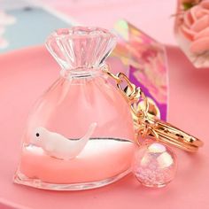 a pink bottle with a white bird keychain sitting on top of it next to a flower