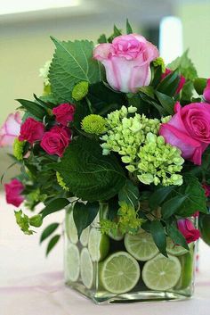 a vase filled with pink roses and limes on top of a white table cloth