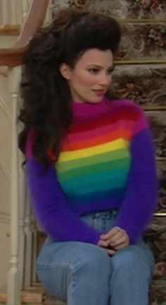 a woman sitting on top of a set of stairs wearing a rainbow sweater and jeans