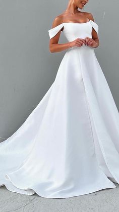 a woman in a white wedding dress standing against a gray wall with her hands on her hips