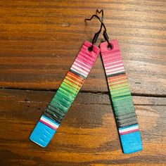 two pairs of colorful wooden earrings hanging from strings on top of a wooden table with wood flooring