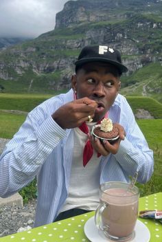 a man in a hat eating food at a table with a cup of coffee and milkshake