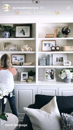 a woman standing in front of a white book shelf filled with pictures and vases