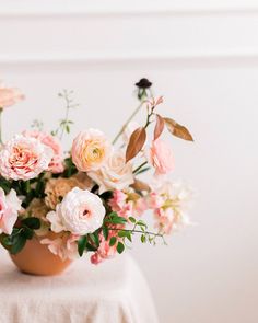 a vase filled with lots of pink flowers on top of a white cloth covered table