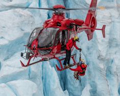 two men in red suits are rapping from a helicopter over an icy glacier wall