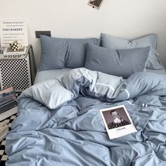 an unmade bed with blue sheets, pillows and a book on the floor next to it