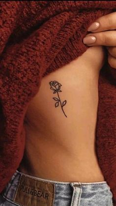 a woman's stomach with a small rose tattoo on her left side ribcage