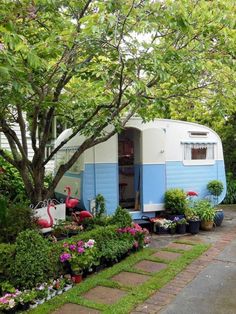 a blue and white trailer parked in front of a tree filled with potted plants