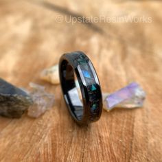 a black ceramic ring with blue opal inlays sits on a wooden surface