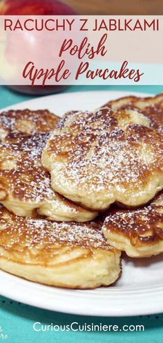 some pancakes on a white plate with powdered sugar and an apple in the background