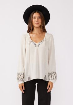 A classic off-white boho blouse with embroidered detail throughout. Embroidered detail Relaxed fit Long raglan sleeve Single-button wrist closure Split v-neckline with tassel ties Smocked neckline Bohemian blouse Classic bohemian details add a cool, effortless touch to this essential fall blouse. Featuring intricately embroidered details and tassel neckties. Perfect for fall and beyond, we love to tuck it into our favorite vintage denim. Model is 5'9, wearing a size S.Style: I-15193W-RRR White Boho Blouse, Blouse With Long Sleeves, Bohemian Blouse, Fall Blouse, Bohemian Blouses, Bohemian Tops, Boho Blouse, Fall Essentials, Embroidered Details