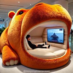 there is a man sitting in the seat of a large teddy bear shaped couch with a television on it