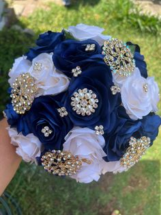 a bridal bouquet in blue and white with brooches on the bottom is being held by someone's hand