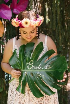 a woman holding a large green leaf with flowers in her hair and the words bride to be written on it