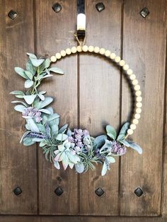 a wreath with flowers and greenery hanging on a wooden door, decorated with beads