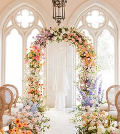 an archway decorated with flowers and greenery in front of two chairs on either side