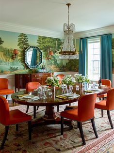 a dining room table with orange chairs and a chandelier hanging from the ceiling