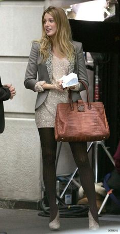 a woman is walking down the street carrying a brown purse and talking to another woman