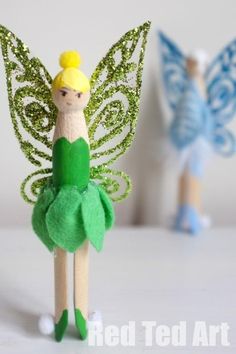 two small wooden sticks with green and blue tinkerbells on them, one holding a yellow flower