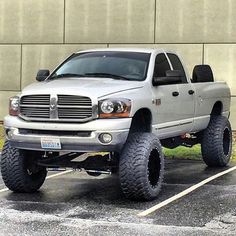 a silver dodge ram truck parked in a parking lot next to a concrete wall and grass