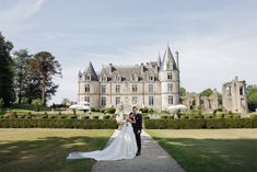 a bride and groom standing in front of a large castle like building with hedges around it