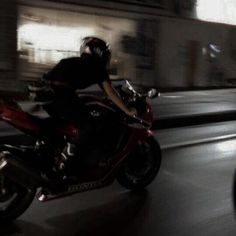 a man riding on the back of a red motorcycle down a city street at night