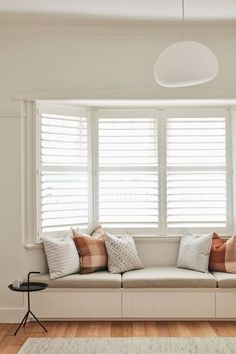 a window seat with several pillows on it in front of a white wall and wooden floor