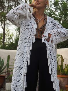 White vintage crochet long jacket up-cycled by Vagabond Ibiza with cute tássel trim. We hand source vintage 1960’s and 70’s unique one off a kind textiles, crochet, knitted and woven and up-cycled them in to one off a kind unique jackets here in our Ibiza studio. Due to the nature of the recycled textiles there could be some slight imperfections but we see this as part of its beauty. Made by hand with love. Size is medium Condition is perfect Long Bohemian Outerwear With Tassels, Bohemian Long Outerwear With Tassels, Bohemian Hand Knitted Cardigan For Beach, Bohemian Hand Knitted White Cardigan, Long Hand Knitted Bohemian Cardigan, Bohemian Hand Knitted Beach Cardigan, Cream Bohemian Knitted Outerwear, Bohemian Winter Cardigan With Crochet Trim, Bohemian Long Sleeve Cardigan With Crochet Trim