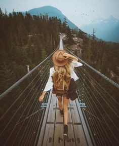 a woman walking across a suspension bridge with mountains in the background