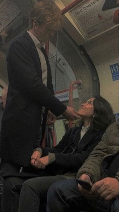 a man in a suit and tie sitting on a bus talking to another woman who is holding a cell phone