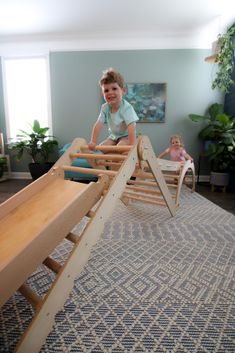 a young boy playing on a wooden slide in the living room with other children sitting around