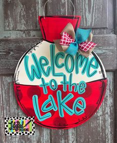 a welcome to the lake sign hanging on a wooden door with a blue and red bow