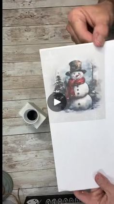 someone holding up a card with a snowman on it and another person's hands