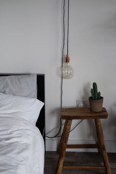 a small table with a plant on it in front of a white wall next to a bed