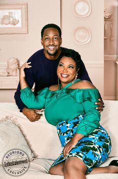 a man and woman sitting on top of a white couch smiling at the camera with their arms around each other