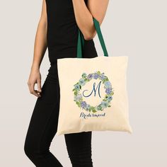 a woman carrying a tote bag with the letter m on it and blue flowers