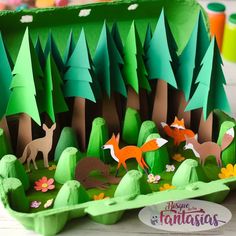 an egg carton with paper cut out of animals and trees in the forest on it