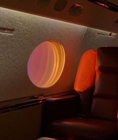 the inside of an airplane with leather seats and round lights in the back wall, on which there is a circular window