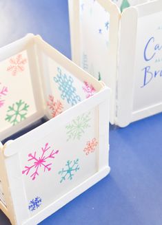 three small white boxes with colorful snowflakes on the front and sides, sitting on a blue surface