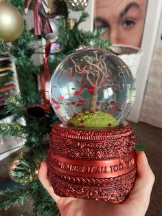 a hand holding a snow globe with a tree in it and words on the inside