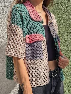 a woman standing next to a wall wearing a crocheted jacket