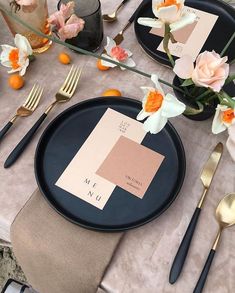 the table is set with black plates, silverware and gold cutlery utensils