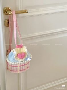 a small purse hanging from the handle of a white door with a pink ribbon around it