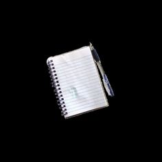 a notepad with a pen on it sitting next to an empty notebook, against a black background