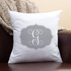 a white pillow sitting on top of a brown chair next to a throw pillow with a monogrammed letter