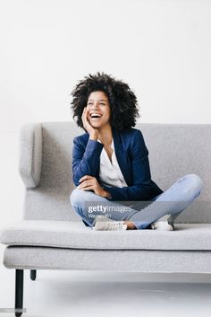 a smiling woman sitting on a couch with her hand to her face stock - fotor